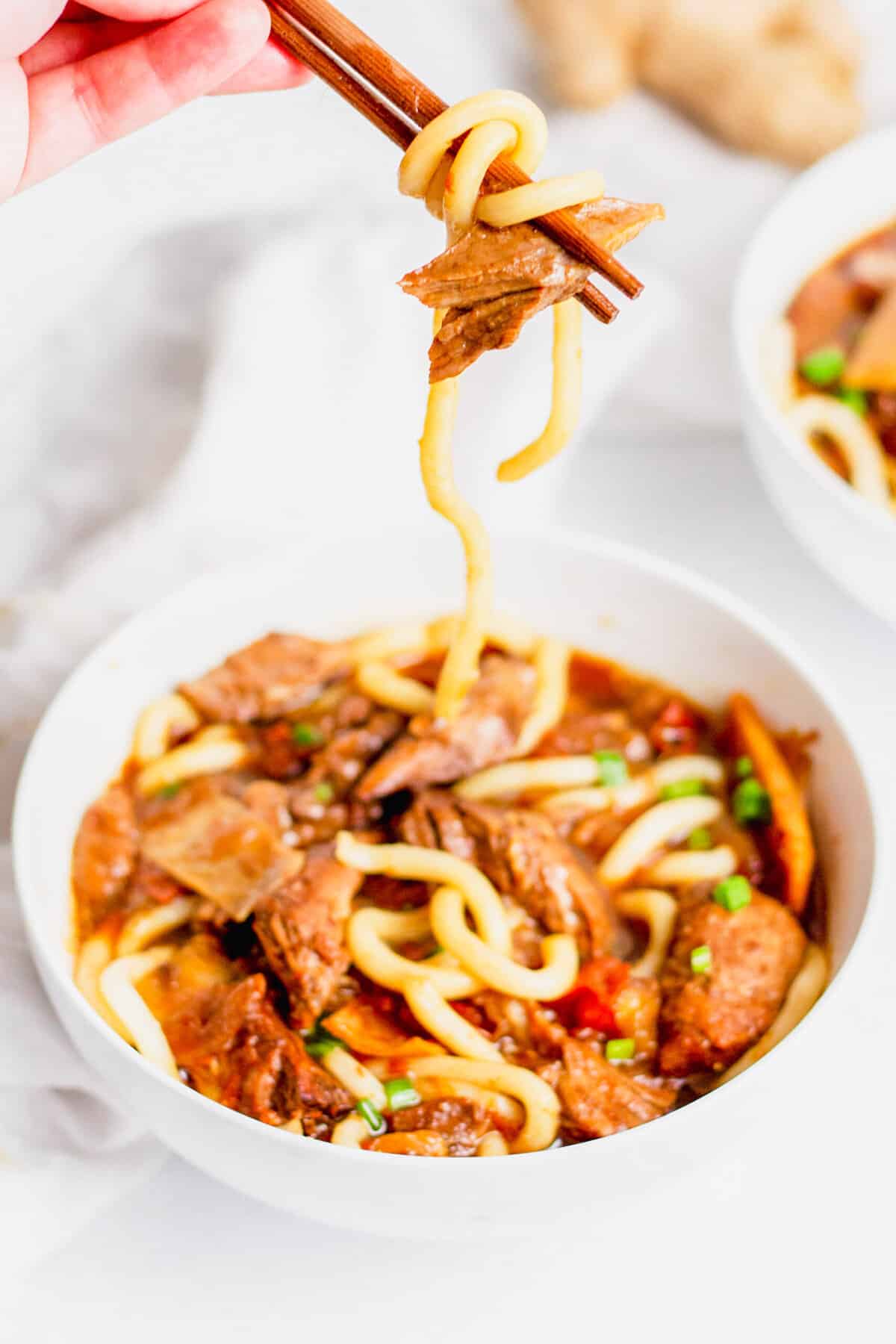 Taiwanese Beef Noodle Soup in white bowl with noodles and beef being picked up with chopsticks