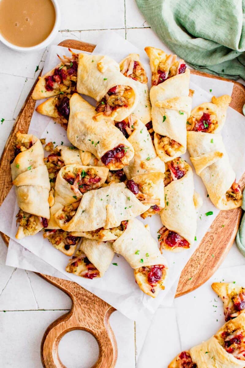 A large serving of rolled Thanksgiving appetizers are presented on a white parchment paper on a wooden surface.