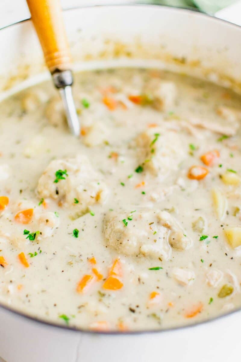 A ladle is placed in a large pot full of creamy soup topped with fresh herbs.