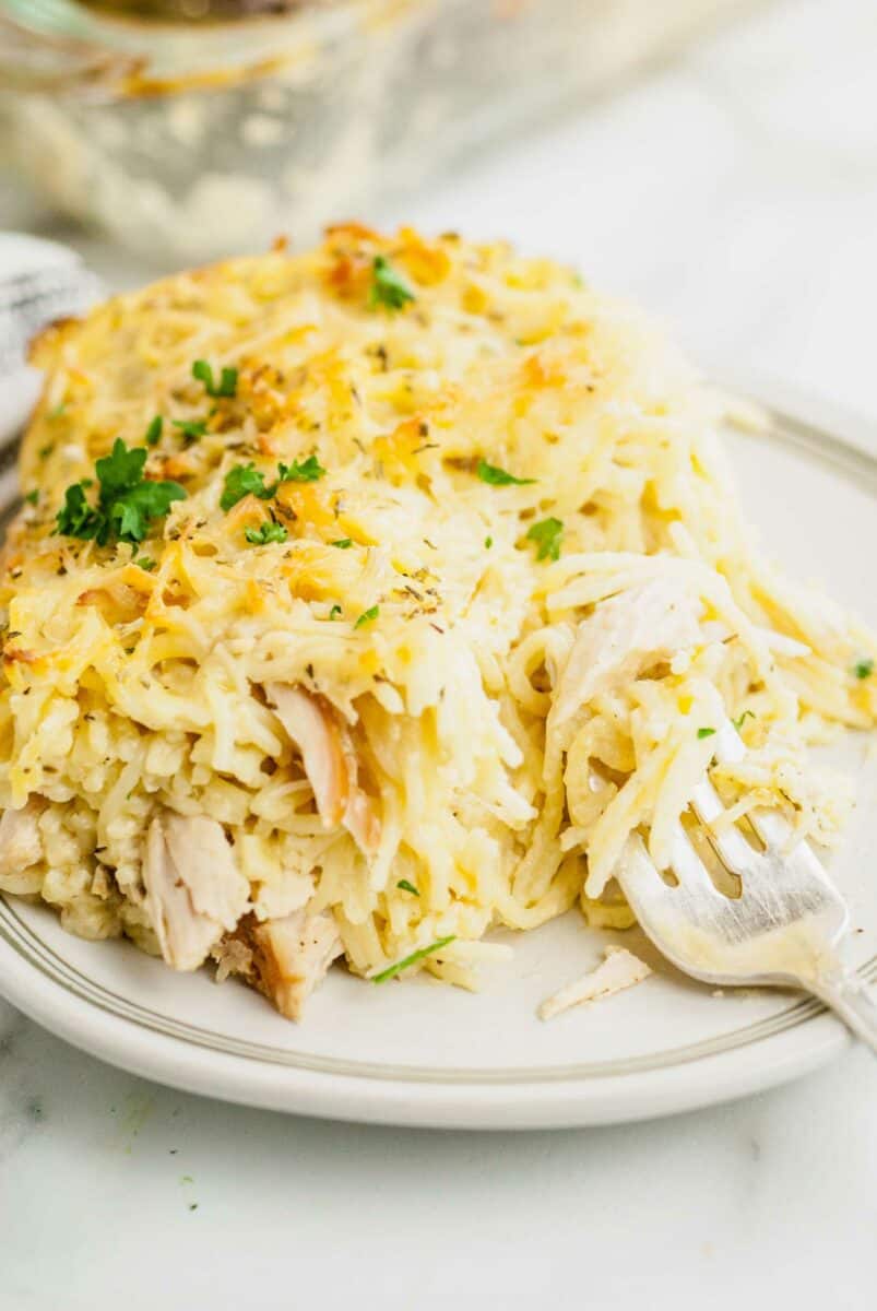 A fork is digging into some turkey and noodles on a white plate.