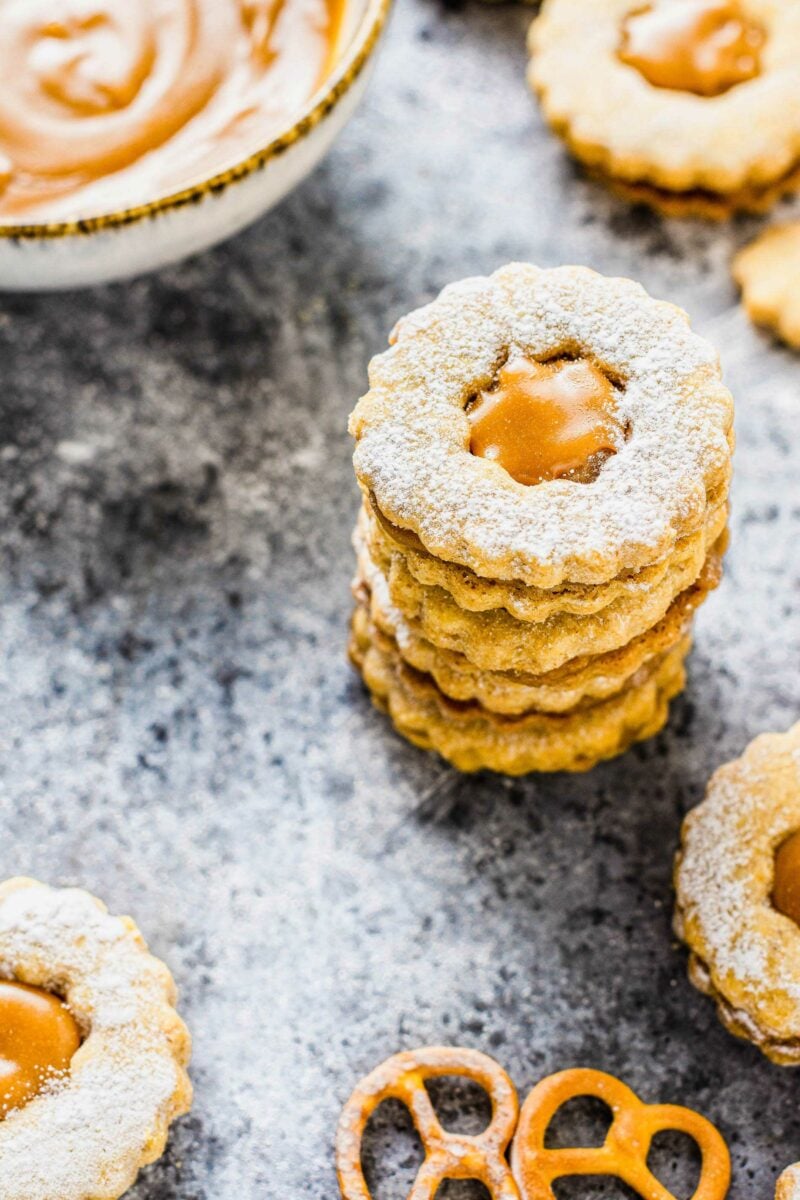 A stack of cookies is presented on a black surface next to pretzels. 