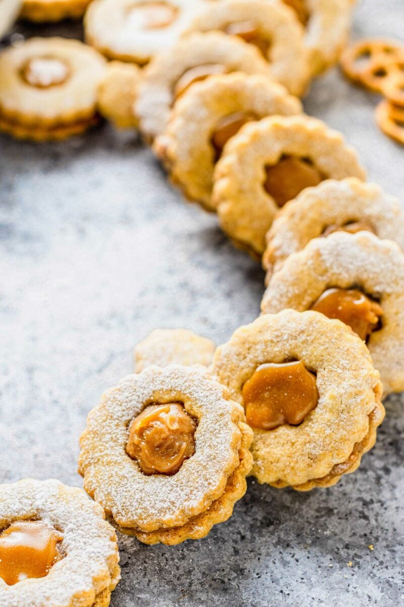 Linzer cookies are presented in a circle on a gray and black surface. 