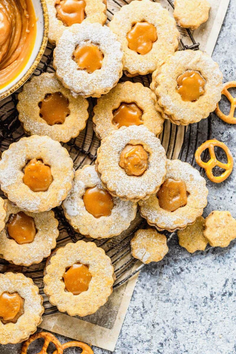 A batch of homemade linzer cookies with caramel filling are placed on a back wire cooling rack.