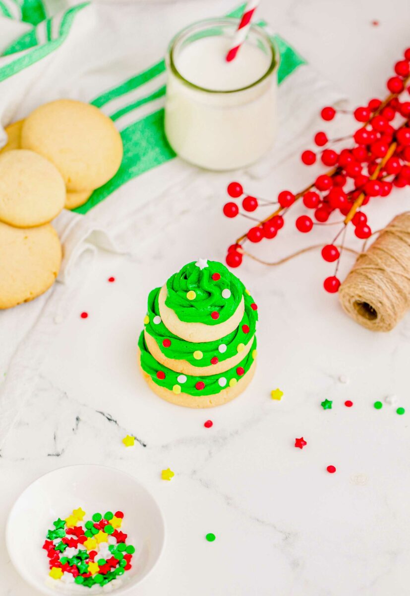 Un-frosted cookies, sprinkles, twine, and berries are all spread around a single Christmas tree cookie. 