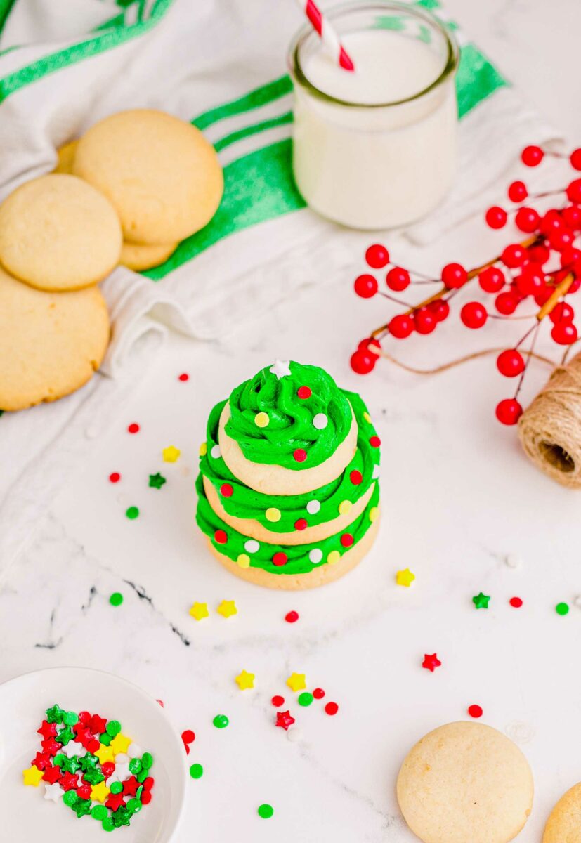 A Christmas tree cookie is presented on a marble surface with sprinkles around it.