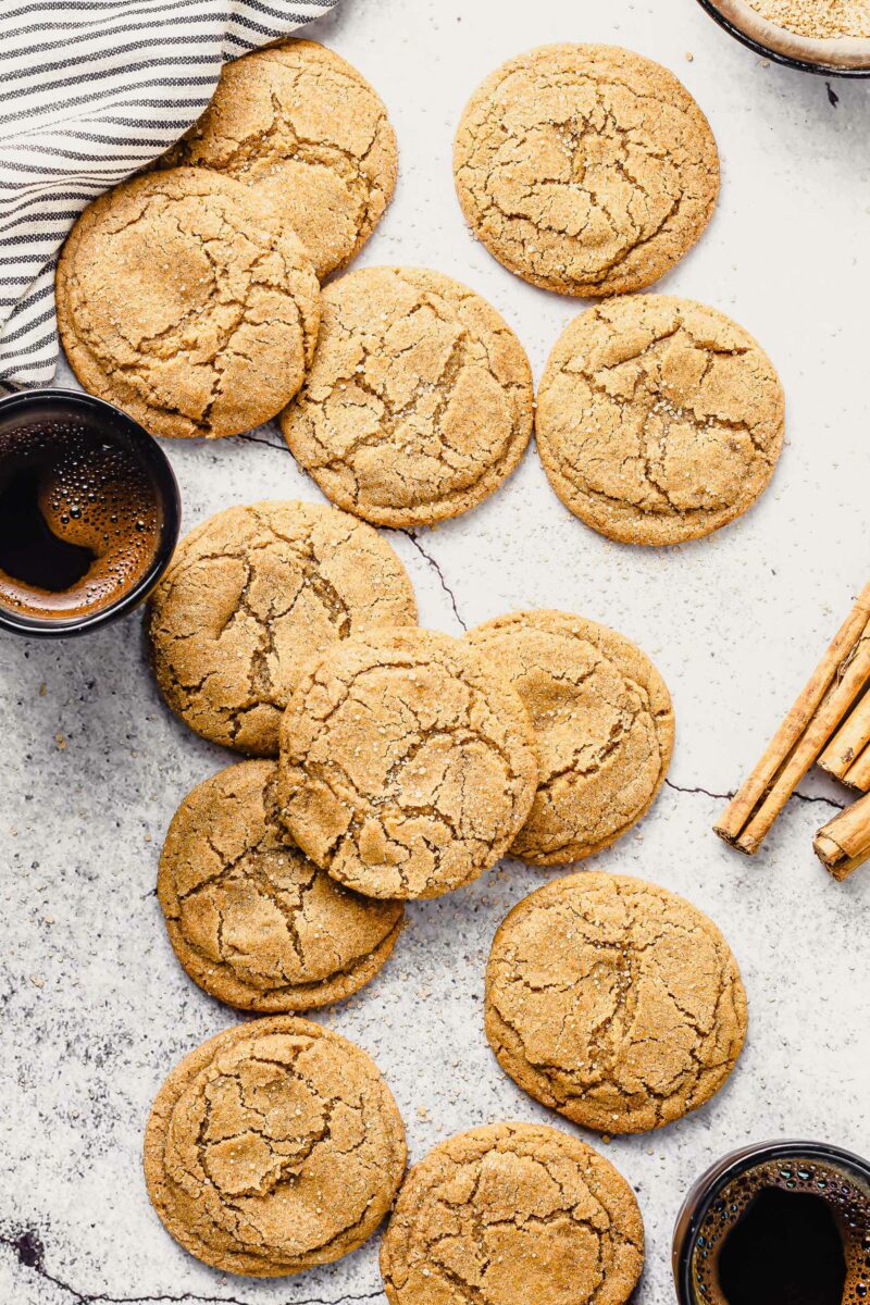 A batch of homemade cookies are presented on a white countertop next to cinnamon sticks. 