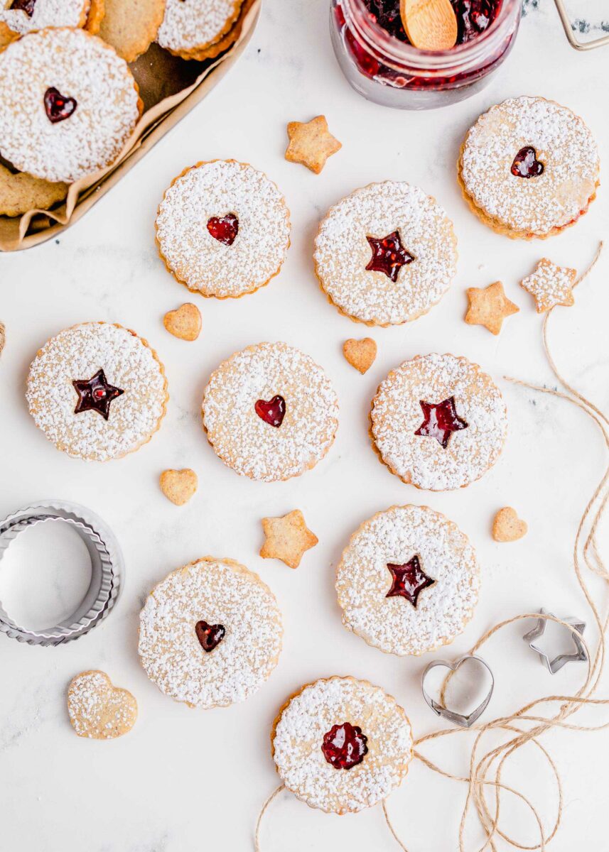A batch of linzer cookies are presented on a white surface next to cookie cutters and twine. 