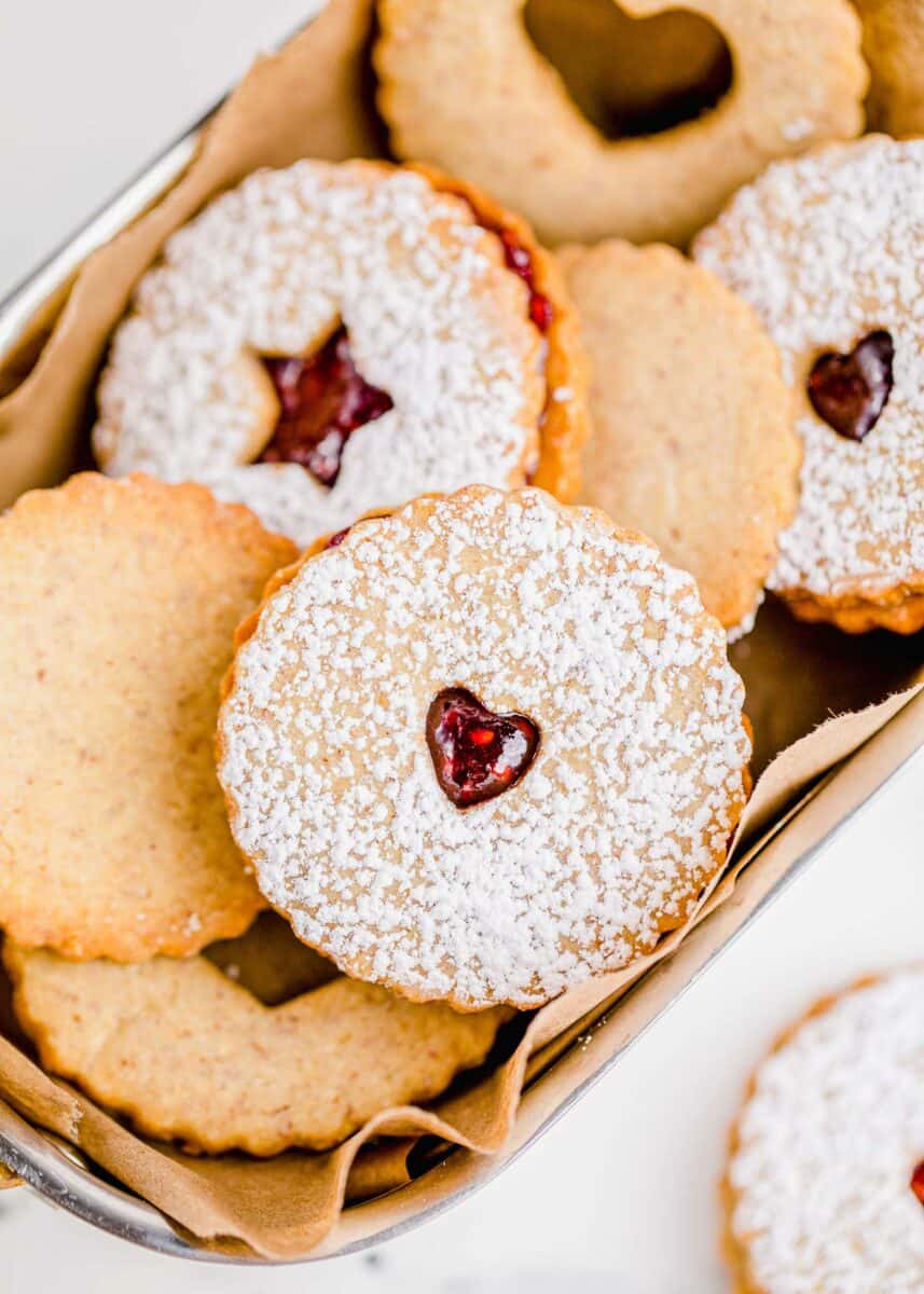 A linzer cookie with a heart cut from the center is placed on top of other cookies. 