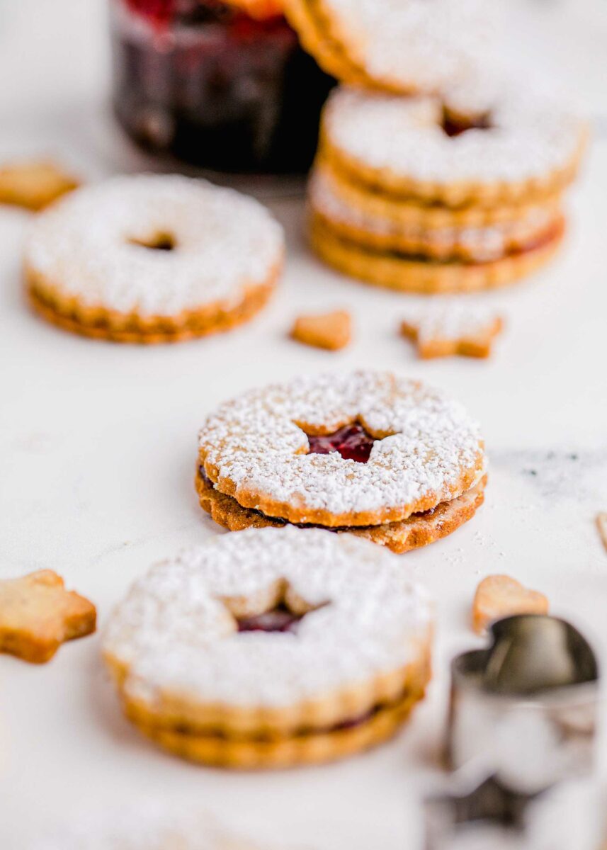 Several dusted linzer cookies are presented on a marble surface. 