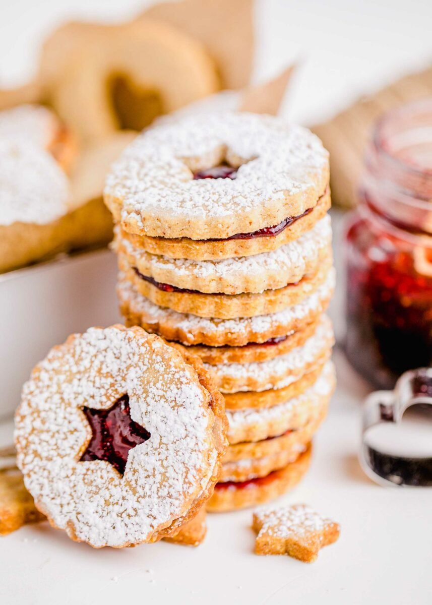 A stack of several linzer cookies are presented on a white marble countertop. 