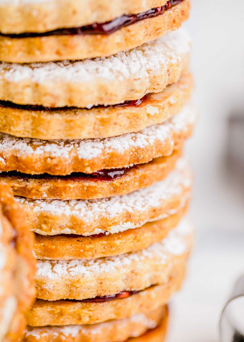 Powder sugar dusted cookies are stacked neatly on top of one another. 