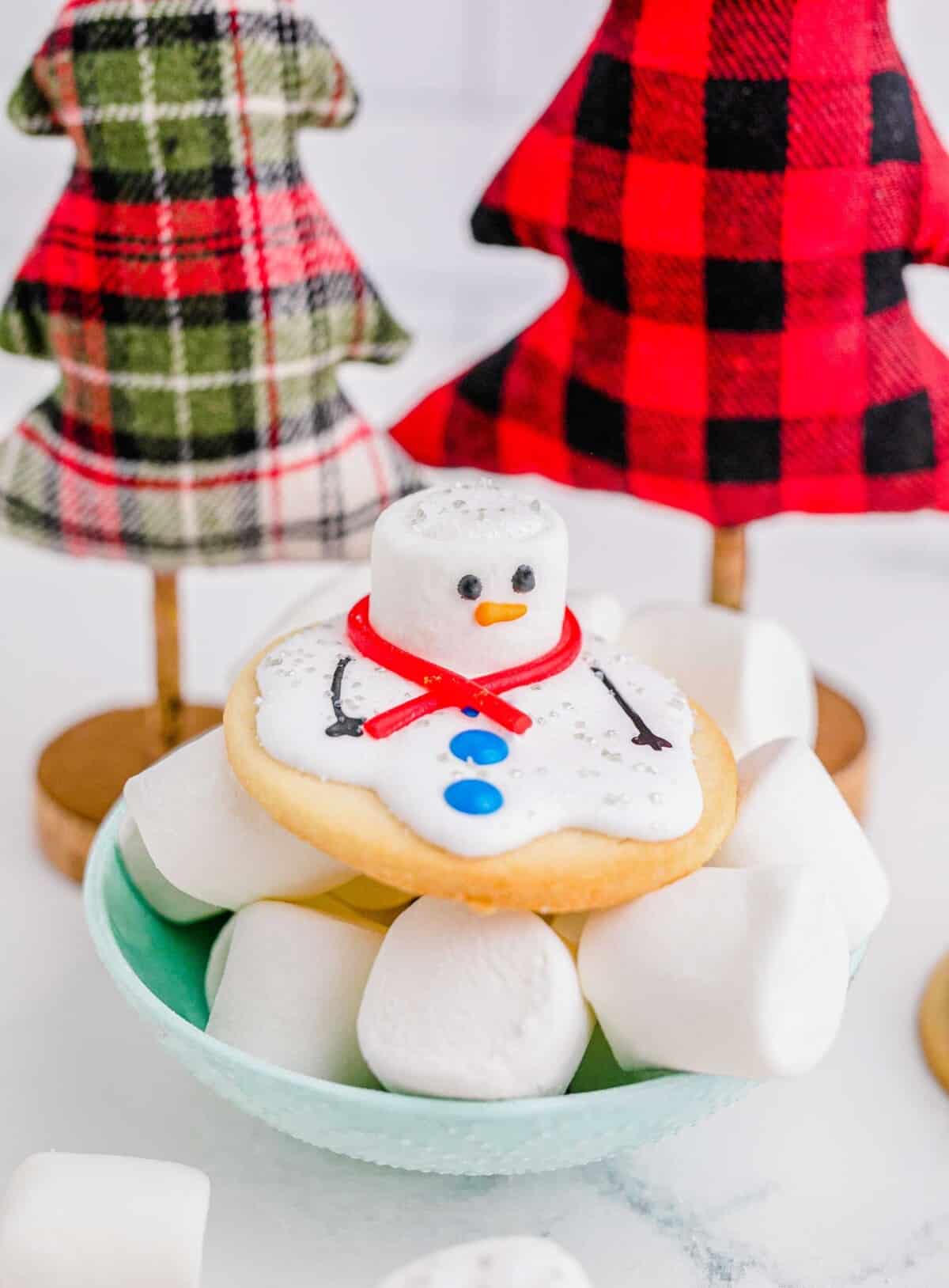 A melted snowman cookie is placed on top of a bowl of marshmallows.