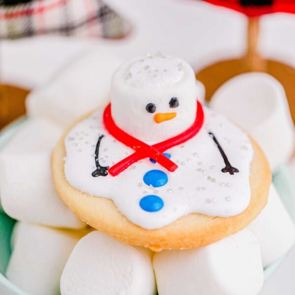 A melted snowman cookie is placed on top of a bowl of marshmallows.