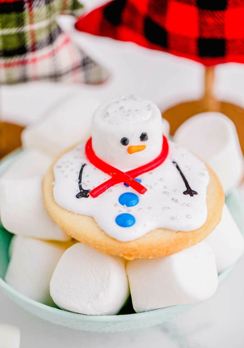 A melted snowman cookie is placed on top of a bowl of marshmallows. 