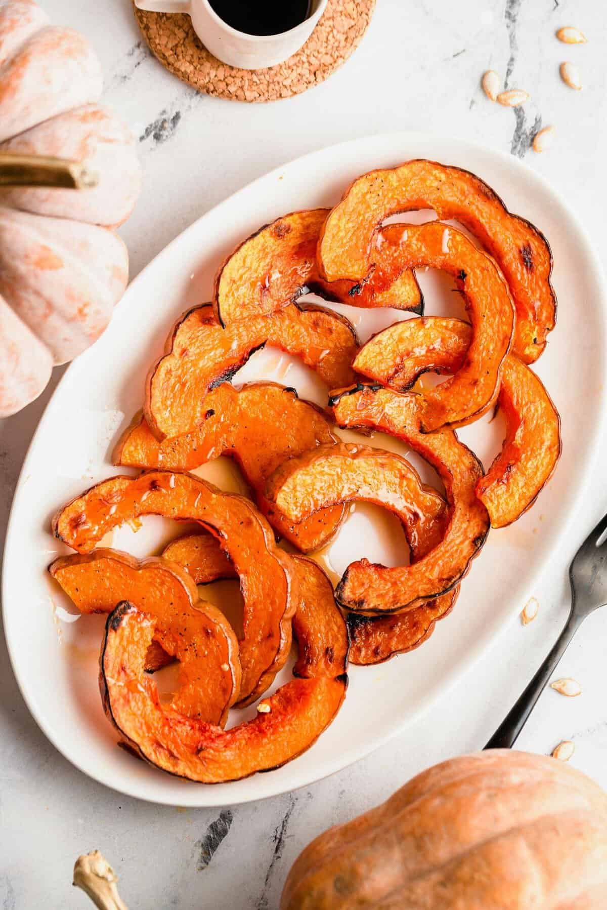 Overhead view of roasted koginut squash slices on white serving platter