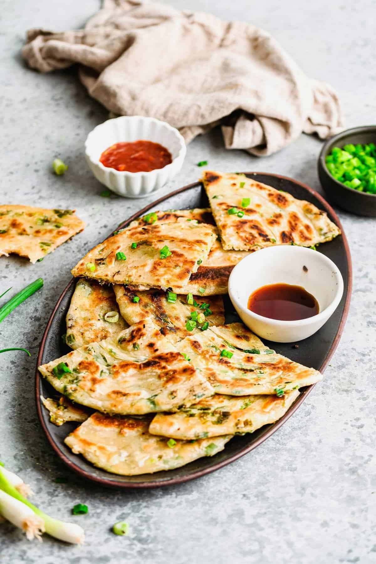 Triangles of scallion pancakes on serving plate with cup of sauce