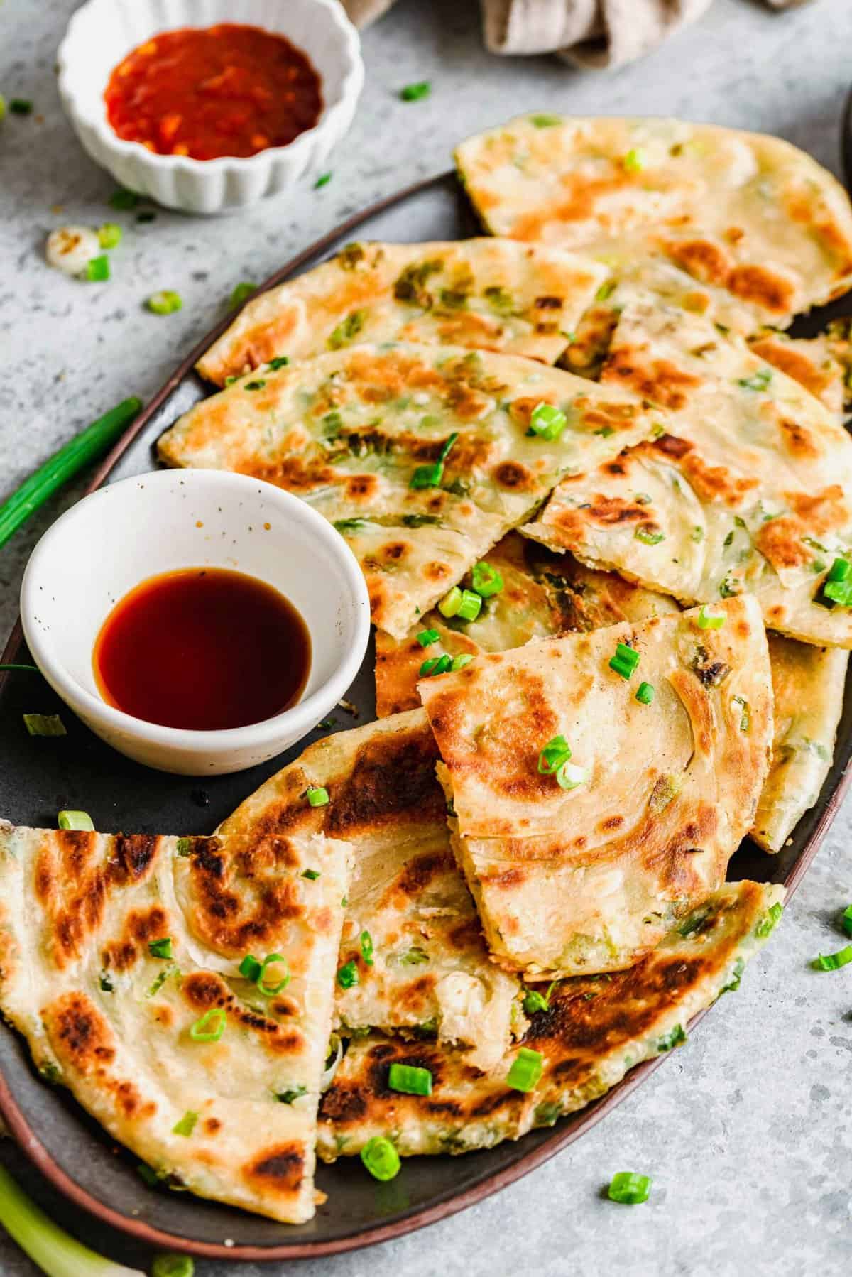 Scallion pancakes cut into triangles on a serving plate with sauce
