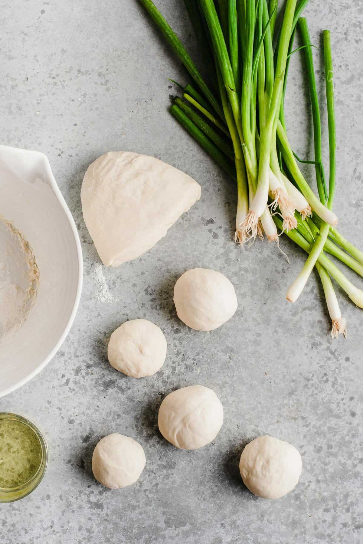 Balls of scallion pancake dough with bunches of scallions and oil