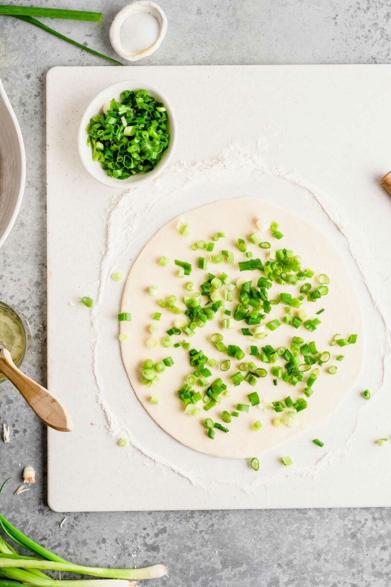 Overhead view of scallion pancake dough covered with sliced scallions