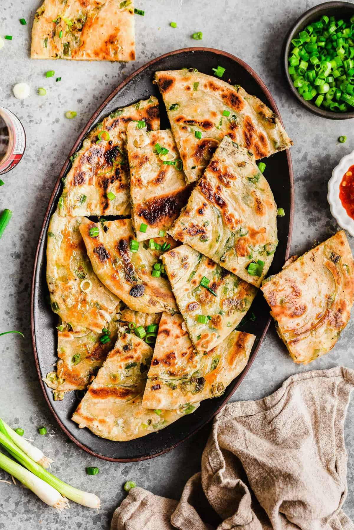 Overhead view of scallion pancakes on platter with scallions scattered over the top