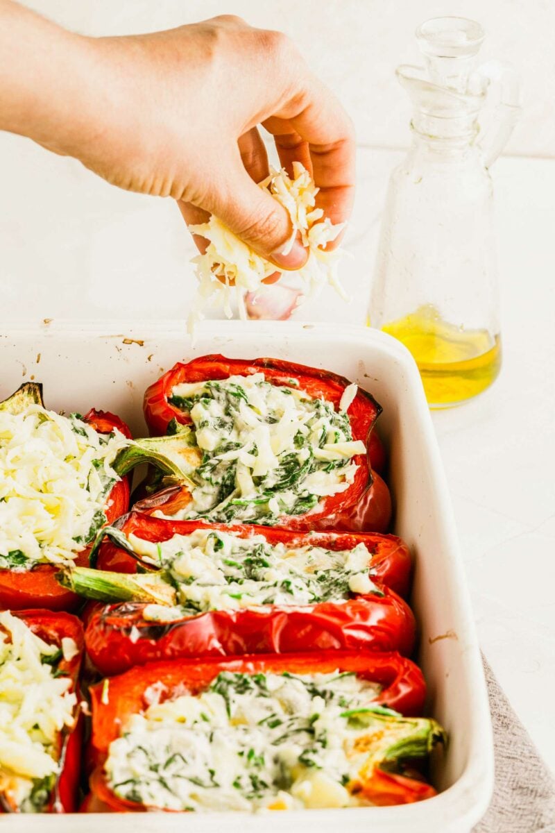 Cheese is being sprinkled over stuffed peppers in a white baking dish.