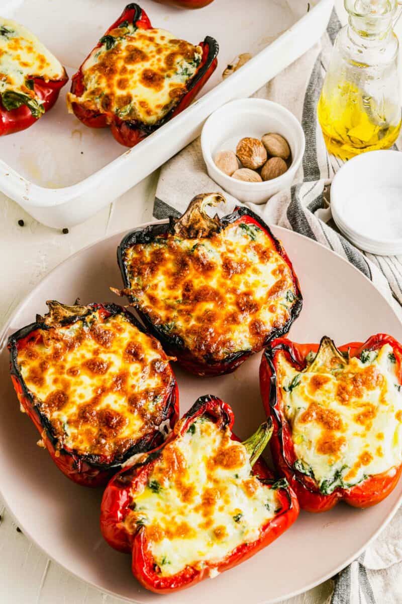 Four cheesy stuffed and cooked red bell peppers are placed on a circular white plate. 
