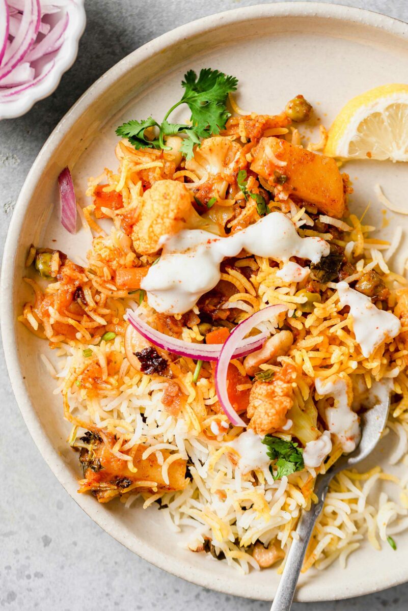 Vegetable biryani is topped with just a little bit of white sauce on a round white plate. 