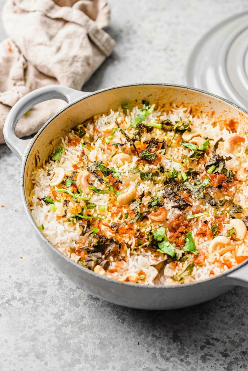 A large white dutch oven is filled with biryani that's garnished with fresh herbs. 