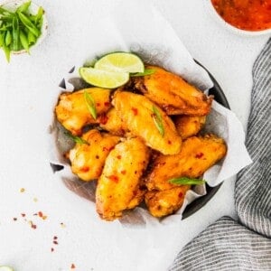 A black bowl lined with parchment paper is filled with chicken wings and garnished with lime slices and green onions.