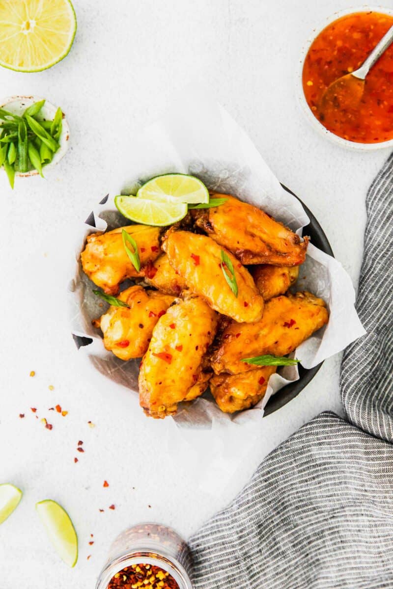 A black bowl lined with parchment paper is filled with chicken wings and garnished with lime slices and green onions. 