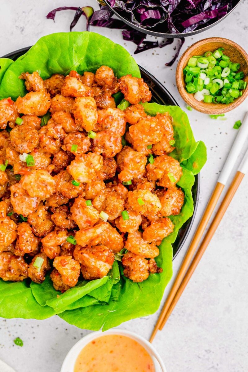 A large serving of bang bang shrimp is presented on green lettuce in a large black serving bowl.