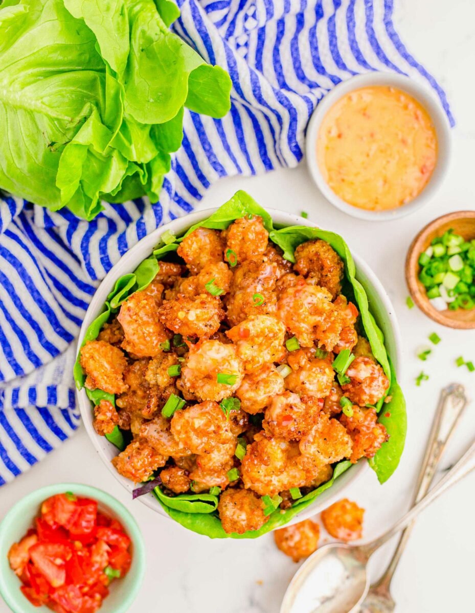 A large white bowl lined with lettuce is filled with cooked bang bang shrimp. 