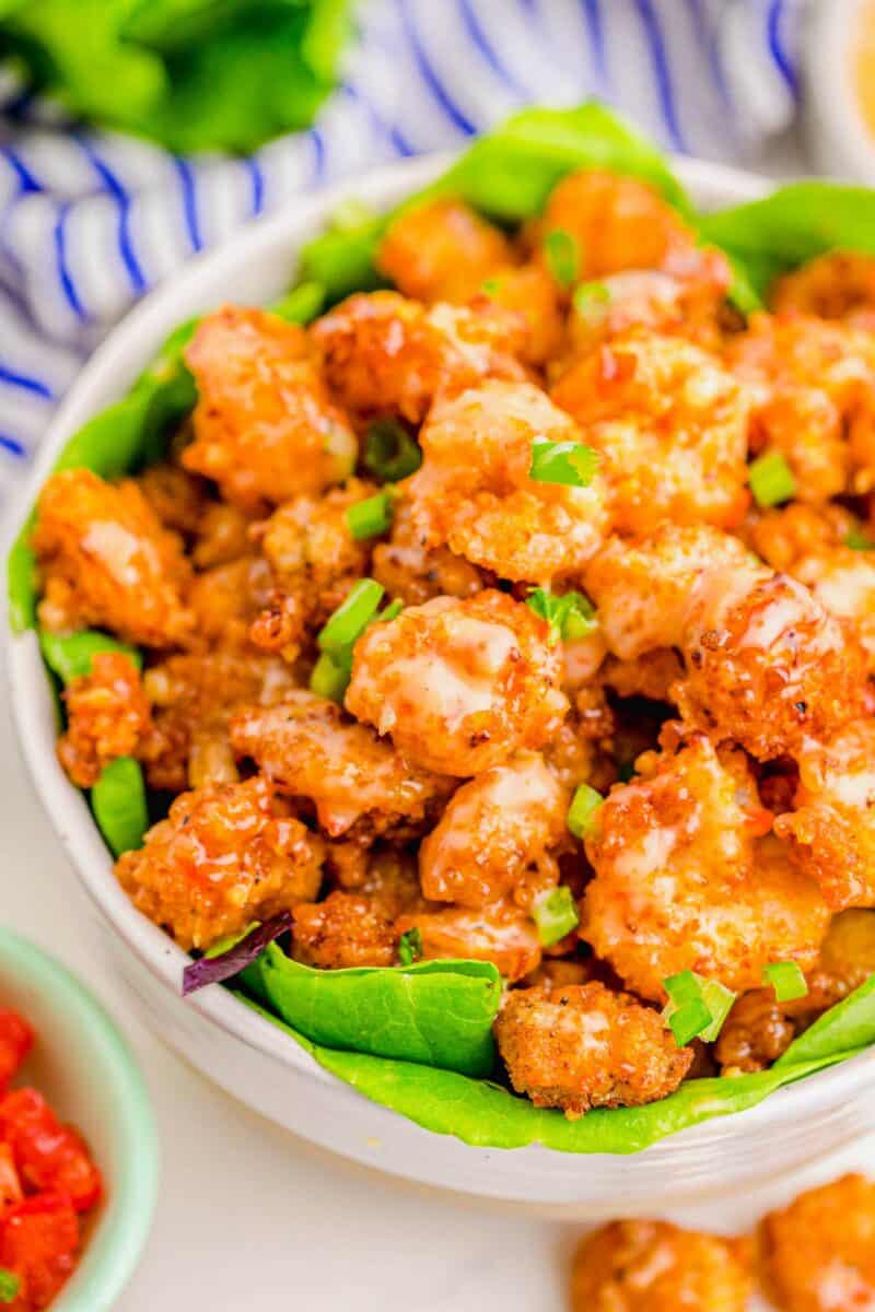 Cooked bang bang shrimp in a large bowl are garnished with chopped green onions. 