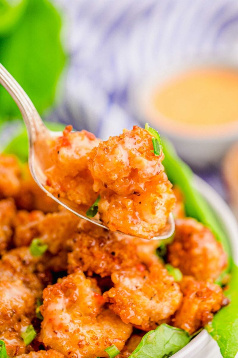 A spoon is lifting a portion of bang bang shrimp from the bowl. 
