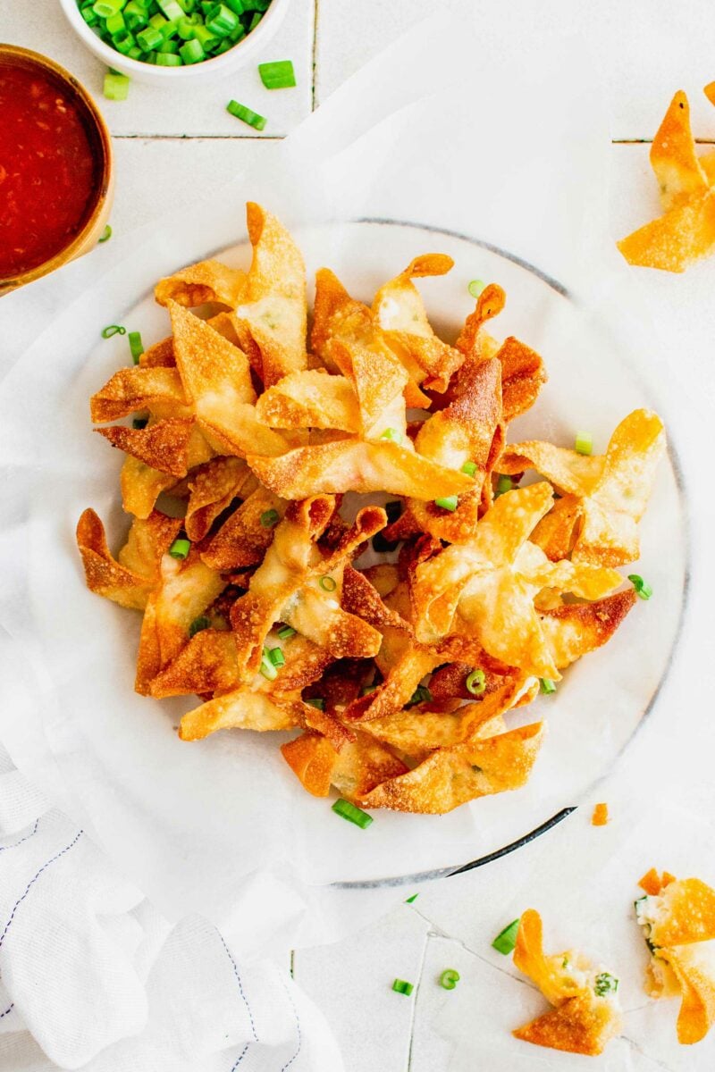 A sheet of parchment paper is topped with cooked crab rangoon and green onions. 