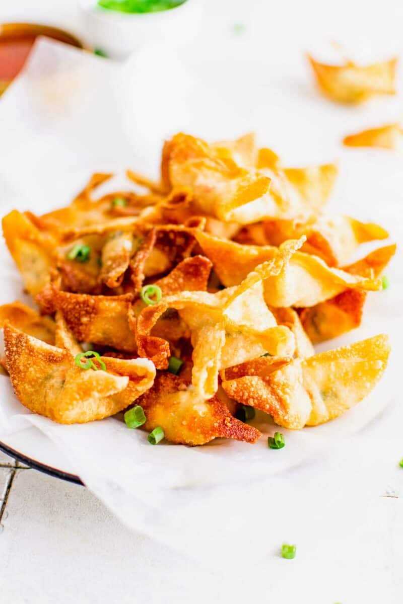 A stack of crab rangoon are presented in a serving dish lined with parchment paper. 