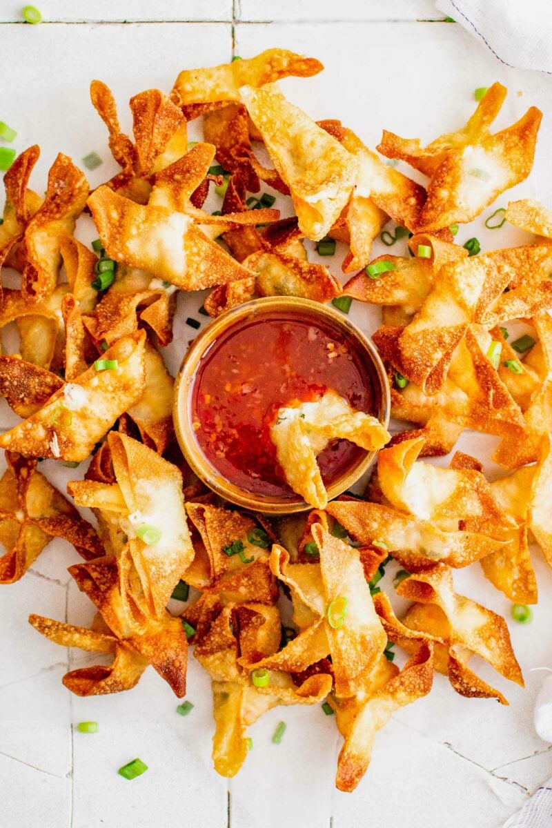 A crab rangoon is being dipped into a small bowl of sweet chili sauce. 