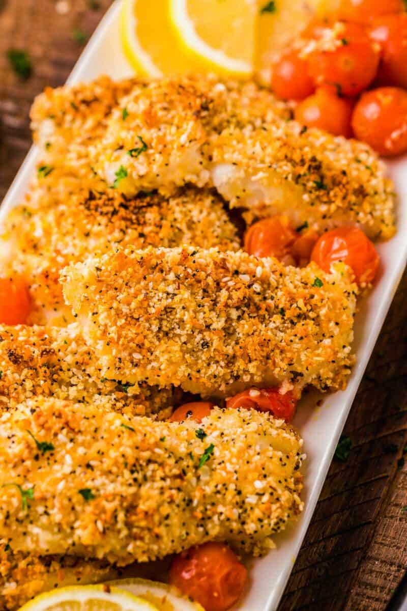 Several crunchy pieces of baked cod are presented with baked cherry tomatoes on a white serving dish.