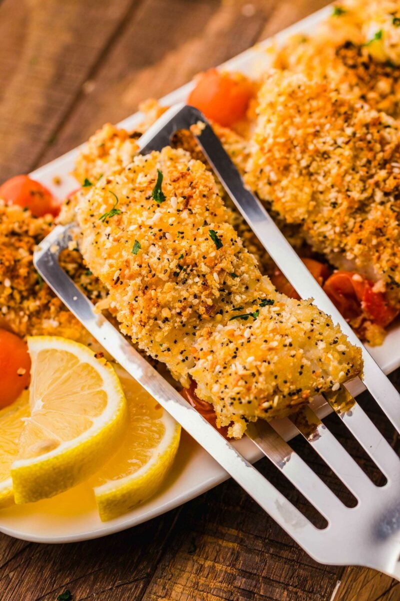 A piece of baked cod is being lifted by a spatula from the serving dish. 