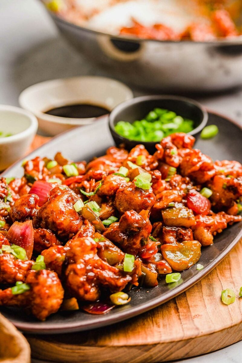 Garnished gobi manchurian is served on a black oval shaped platter. 