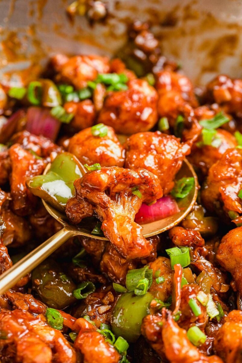 A metal serving spoon is lifting a portion of gobi manchurian from the pot. 
