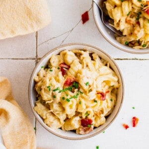 Overhead view of cheesy chicken pasta in bowls, garnished with bacon and chives