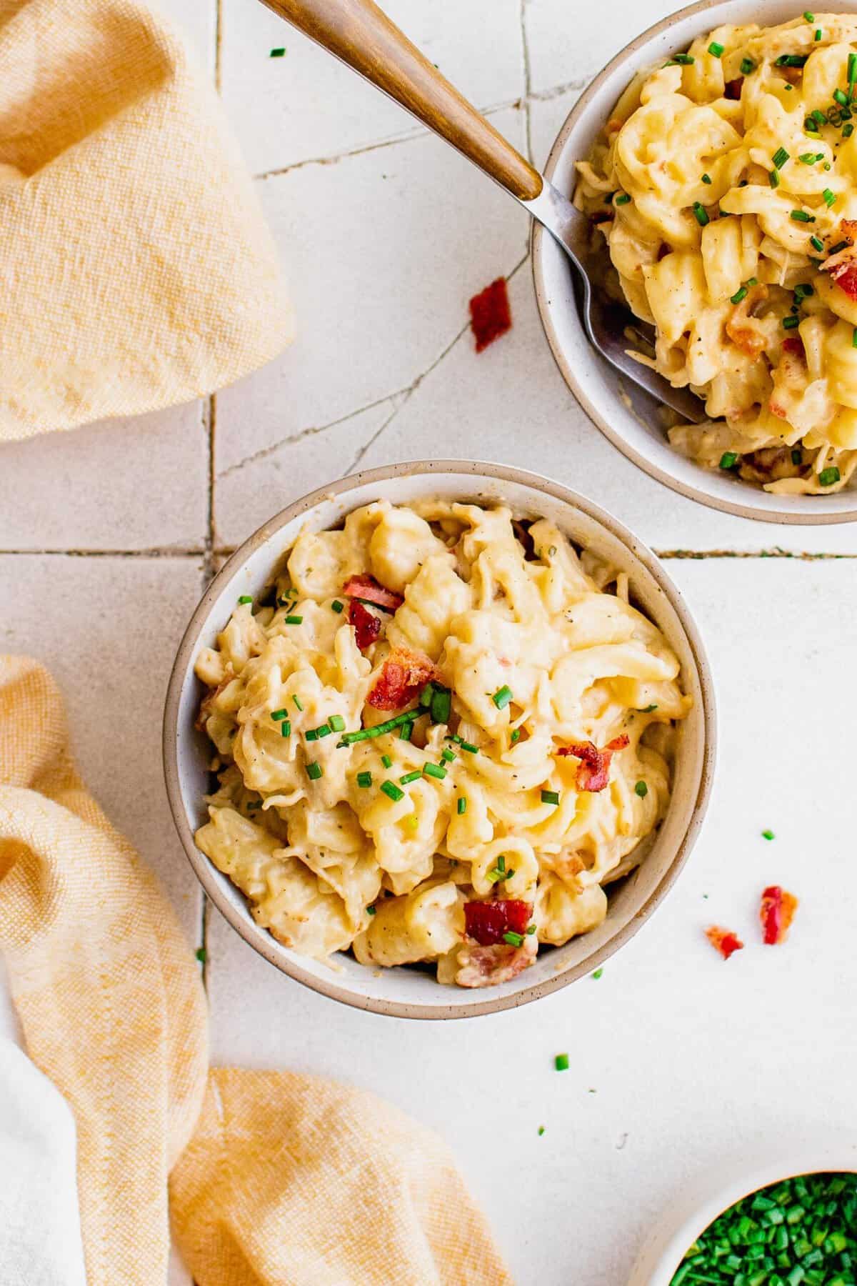 Overhead view of cheesy chicken pasta in bowls, garnished with bacon and chives