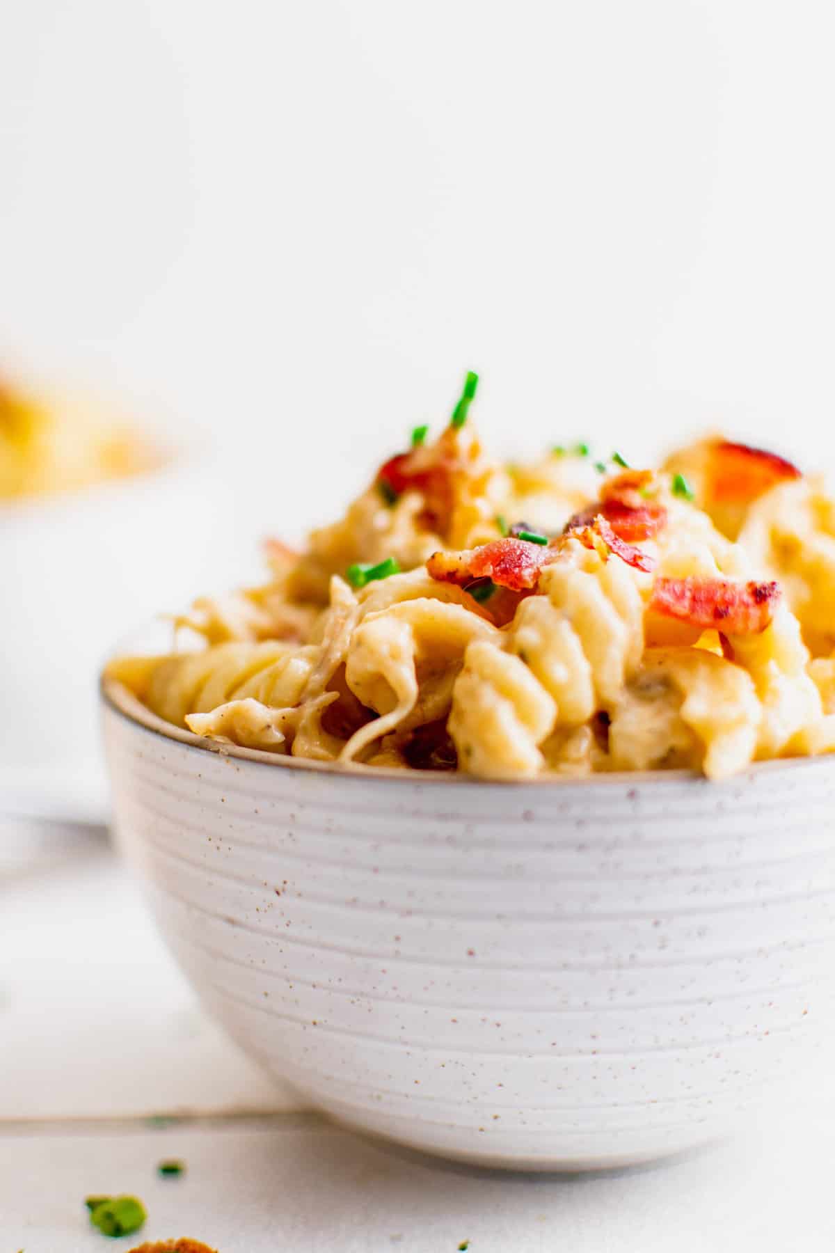 Bowl filled with crack chicken pasta, garnished with chives and bacon