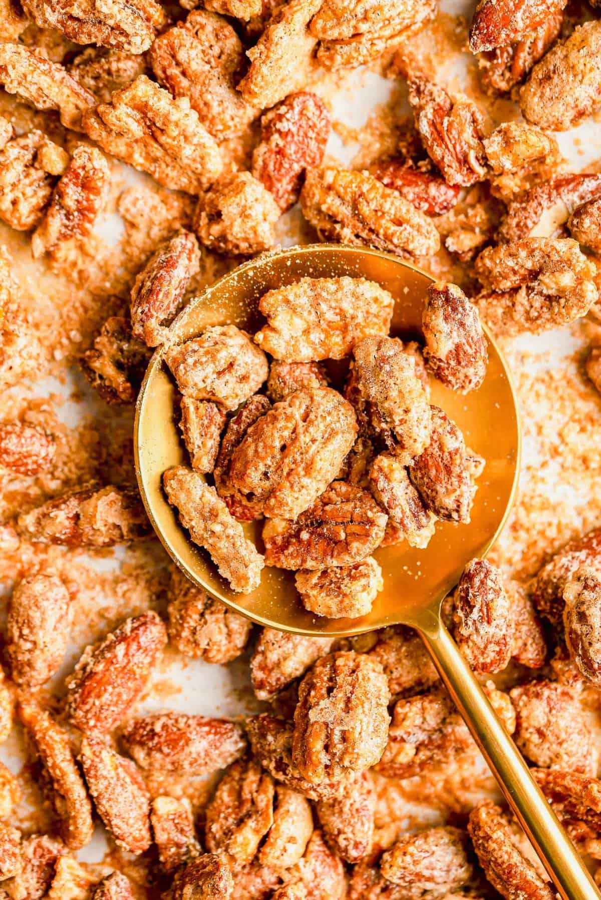 Round gold spoon resting on sheet pan, filled with spiced nuts