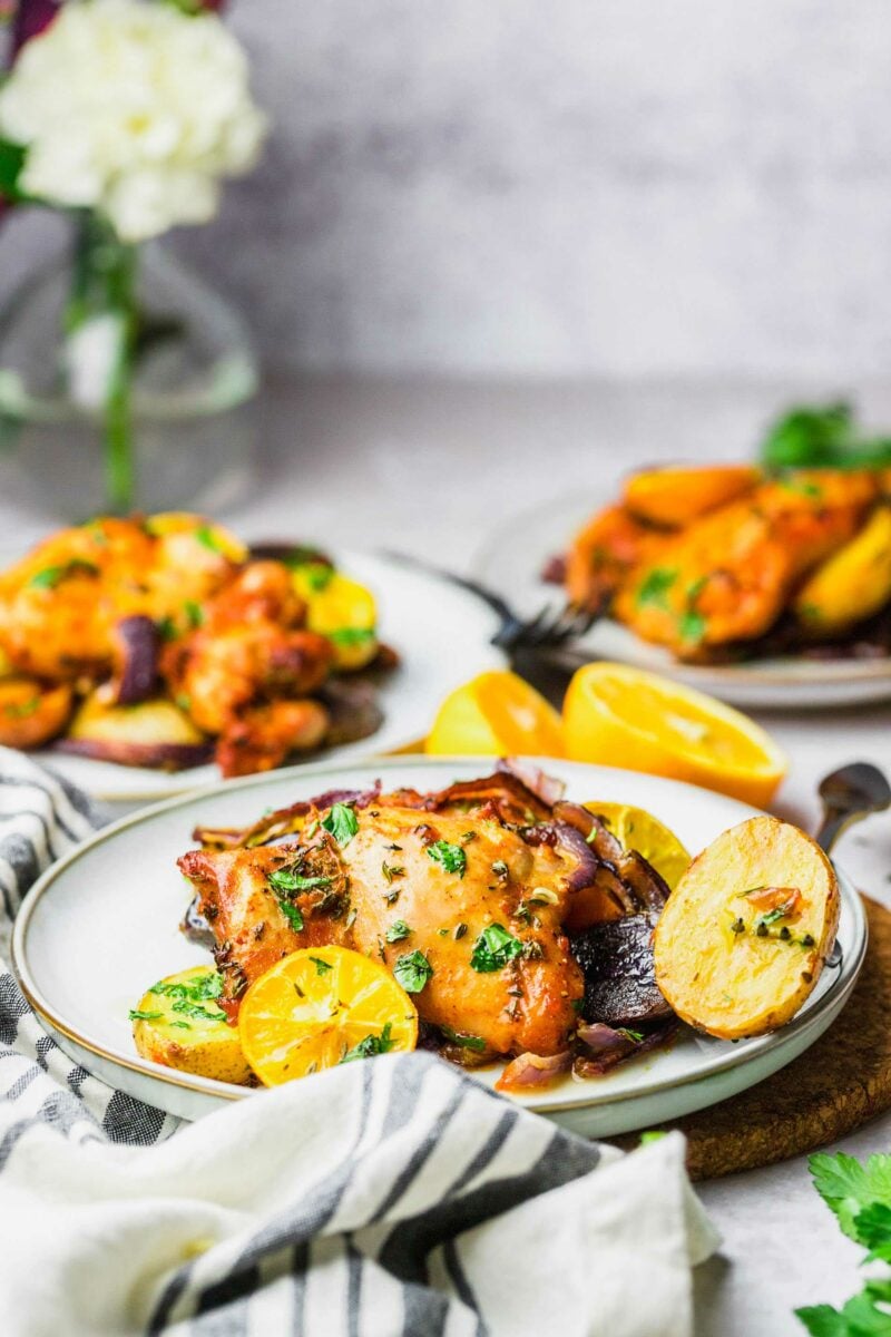 Potatoes, lemons, and chicken thighs are presented next to a fork on a white plate. 