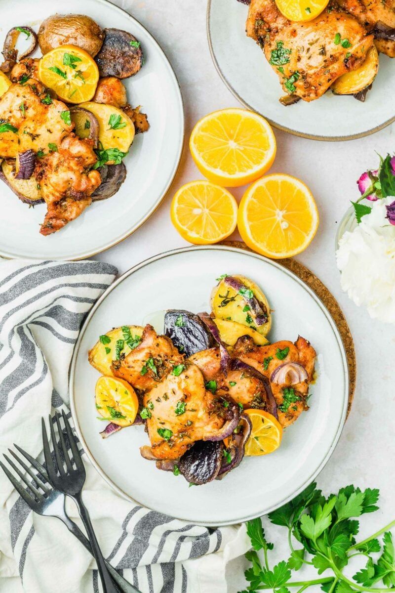 A plate is presented with chicken thighs, onions, lemons, and potatoes. 