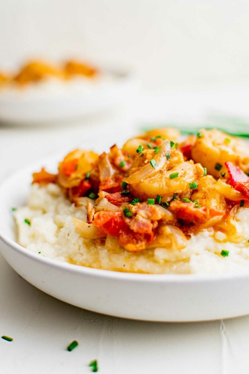 Chives garnish a serving of cooked grits and shrimp in a white bowl. 