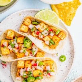 Three tofu tacos on plate with lime wedge and tortilla chips