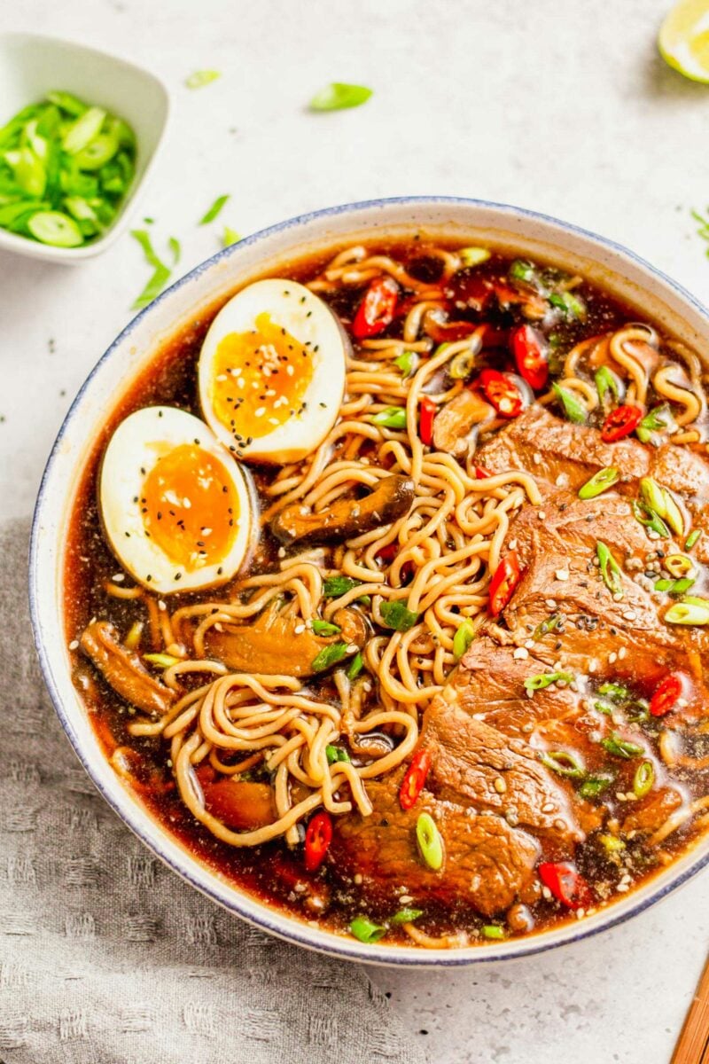 A bowl filled with ramen noodle soup is garnished with black and white sesame seeds.